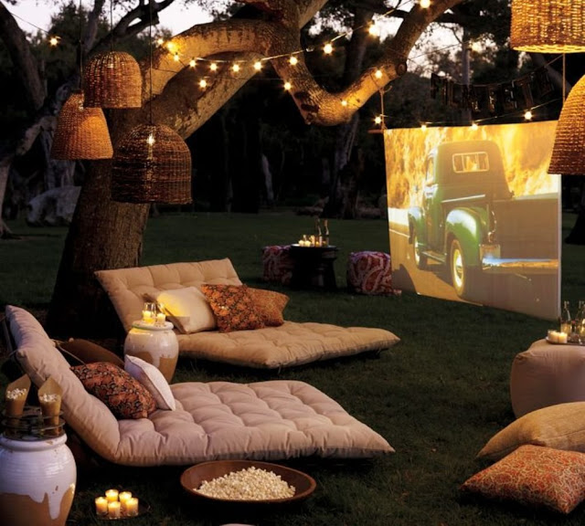 Aménagement d'un cinéma en plein air avec coussin, pop corn, guirlande lumineuse et grand écran dans le jardin : c'est l'été